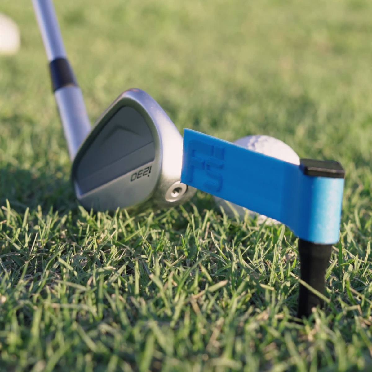 Close-up at ground level of an iron behind the ball, with a FlagSwing staked just beyond the ball and its flag pointing back at it.