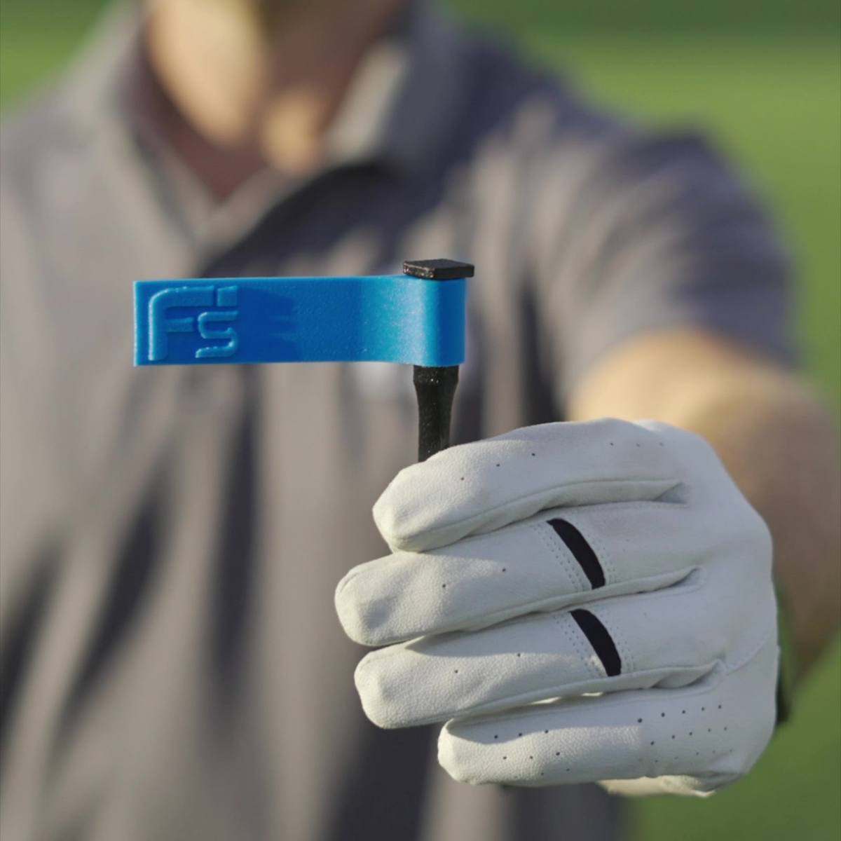 A FlagSwing held in a golfer’s gloved hand, a small black stake topped with a blue flag.