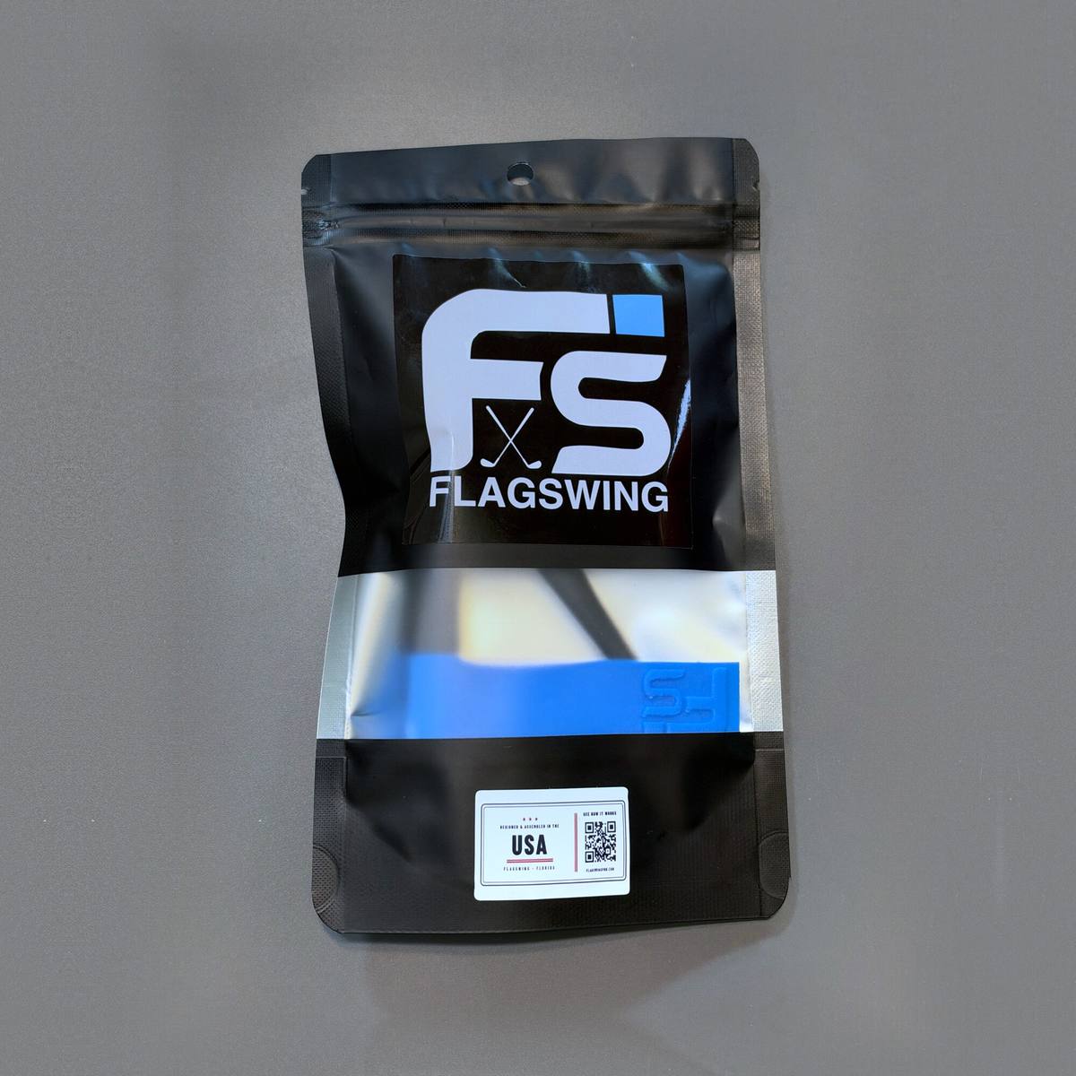The front of the FlagSwing pouch, black with the FlagSwing logo, a window showing a blue flag inside, and the origin label near the bottom.